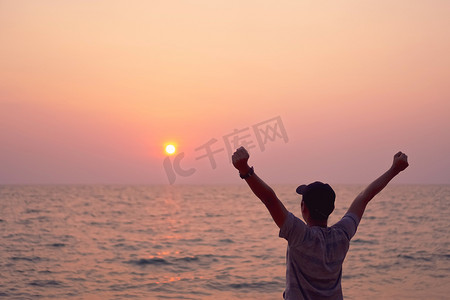 男人举起手来迎接蓝天和夏日海滩背景的天空自由概念。