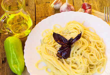 白色盘子里的意大利面，旧木桌上放着罗勒，玻璃罐里放着蔬菜和橄榄油
