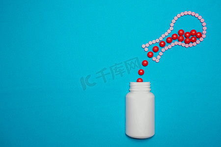 创意瓶中摄影照片_红色药丸从由药丸制成的圆底烧瓶中溢出，进入蓝色背景的白色瓶子中。