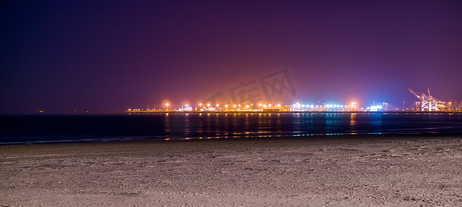 Blankenberge 海滩的海岸线被夜晚照亮，远处工业区的五颜六色的灯光