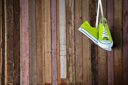 绿色的运动鞋摄影照片_木墙上挂着一双新的绿色运动鞋