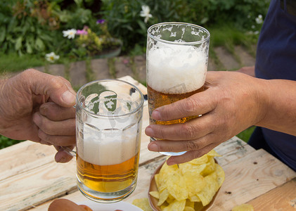 浅色木板摄影照片_手拿着啤酒、薯条和香肠放在浅色木板上的眼镜，人们在周末放松，十月节