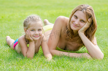 年轻的母亲和五岁的女儿躺在绿草上，看着画框