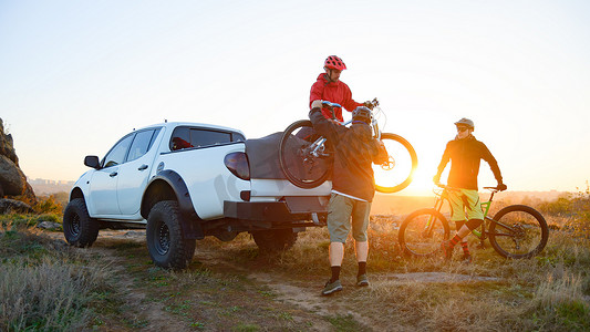 越野摄影照片_朋友们在日落时从山区的皮卡越野卡车上取下 MTB 自行车。