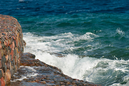 有波纹摄影照片_美丽清澈的绿松石海水面照片，石质海景背景上有波纹和明亮的飞溅，水平图片