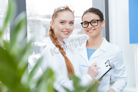 穿着实验室外套和眼镜的年轻女科学家做笔记并对着镜头微笑
