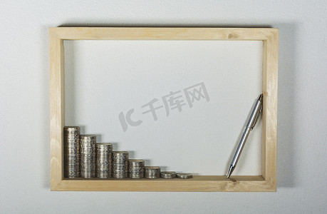 白色墙壁背景上的木制框架中用钢笔堆叠硬币。
