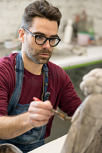穿着围裙的陶艺家在明亮的陶瓷车间从事粘土雕塑工作的肖像。