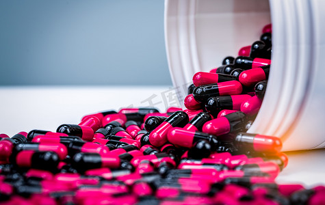 禁忌症摄影照片_粉红色、黑色的胶囊药丸从白色塑料瓶容器中溢出。