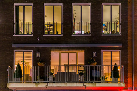美丽的公寓阳台装饰着植物，夜间点亮的窗户，现代荷兰建筑