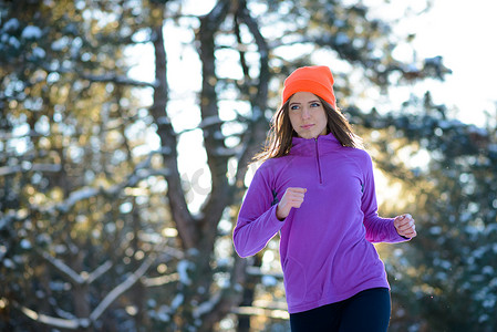 在阳光明媚的寒冷日子里，年轻女子在美丽的冬季森林中奔跑。