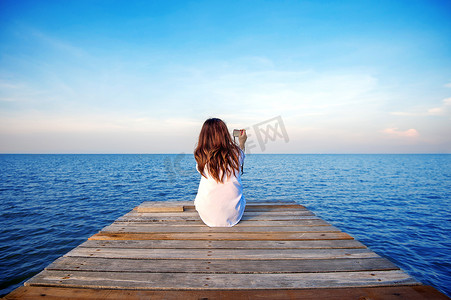 女孩独自坐在海上的一座木桥上，手拿着相机。