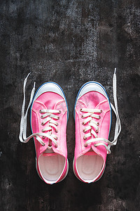 深色混凝土上饰有未系鞋带的紫粉色淡紫色运动鞋