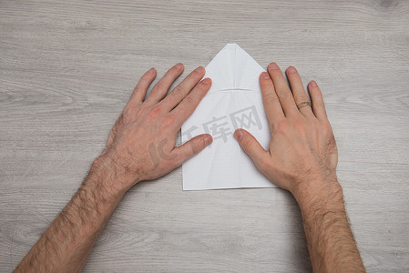 折纸飞机摄影照片_如何在带手臂的木桌上逐步制作折纸纸飞机的照片说明。