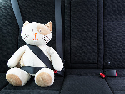 小汽车玩具摄影照片_毛绒玩具猫用安全带固定在汽车后座上，路上安全。