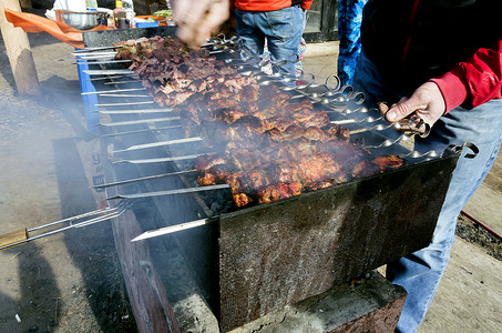 露天烤架上烤串上的肉，厨师可见的手