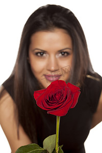 拿着一朵红色玫瑰的愉快的美丽的少妇