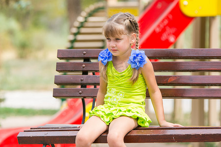 坐在操场背景长椅上的心烦意乱的五岁女孩的画像