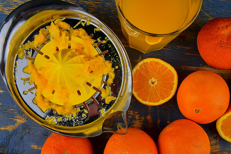 橘子、橙子、一杯橙汁和蓝色木质背景上的手动柑橘榨汁机。