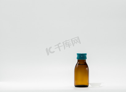 禁忌症摄影照片_在琥珀色瓶的药糖浆与空白标签和茶匙在白色背景。