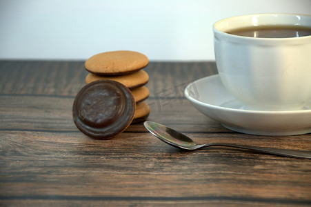 木桌上放着一杯放在瓷碟上的红茶、一把勺子和一堆巧克力海绵饼干。