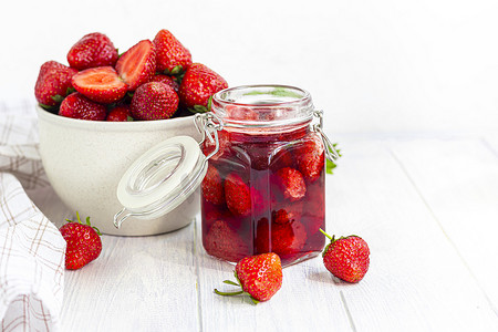 在新鲜草莓旁边的玻璃罐中的草莓酱。