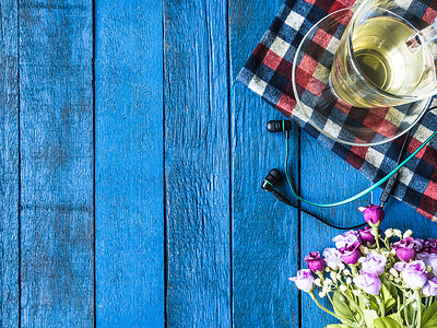 蓝色的茶杯摄影照片_蓝色木桌背景上带花和耳机的茶杯的顶视图。