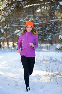 在阳光明媚的寒冷日子里，年轻女子在美丽的冬季森林中奔跑。