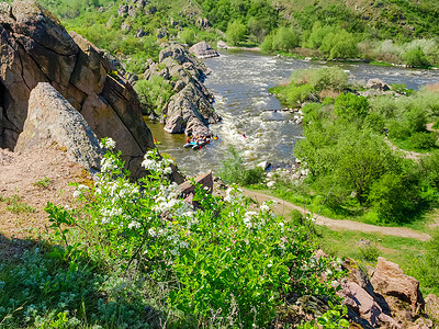 瀑布水流摄影照片_有急流、岩石岸和开花的樱桃的河在前景