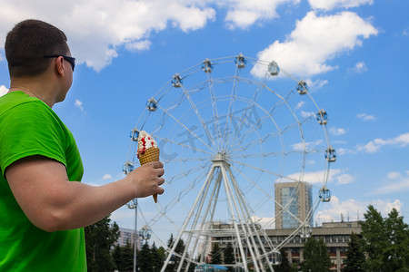一个手里拿着冰淇淋的男人站在游乐园里看着摩天轮