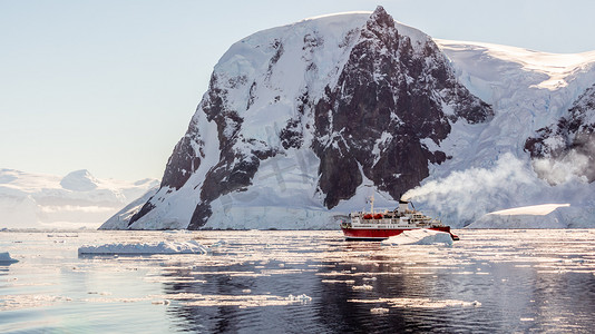 漂流在有巨大的岩石的冰山中的红色巡航汽船