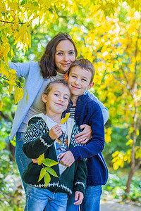 有两个孩子的母亲在秋黄树下微笑