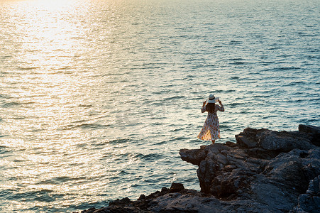 年轻女子站在岩石顶部，看着四长岛的海边和日落。