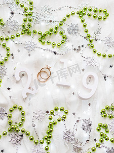 圣诞节和新年背景与数字 2019、绿色装饰、结婚戒指和灯泡。