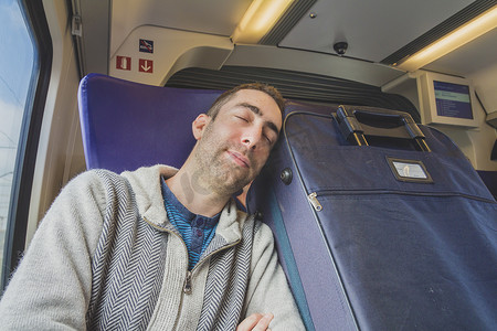 年轻人乘火车旅行，睡在旁边的蓝色手提箱上