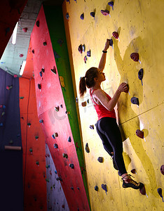 年轻活跃的女性在攀岩馆的彩色人造岩石上抱石。