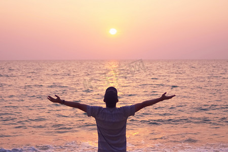 男人举起手来迎接蓝天和夏日海滩背景的天空自由概念。