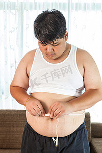 损失摄影照片_拿着卷尺的亚裔胖子