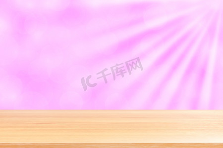 粉红渐变摄影照片_空木桌地板上柔和的粉红色散景灯光束闪耀渐变背景，木板空在粉红色散景彩色灯光照耀下，粉红色彩色散景灯渐变柔和，用于横幅广告