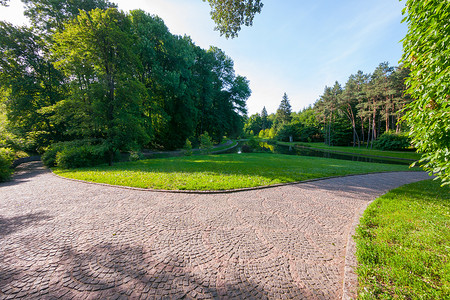 夏日多云的日子里，这条小路铺在美丽的绿色公园里，铺着石头路面。