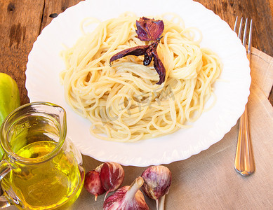 白色盘子里的意大利面，旧木桌上放着罗勒，玻璃罐里放着蔬菜和橄榄油
