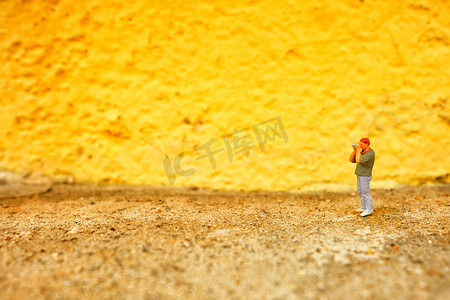 微型人物摄影师与黄色彩绘混凝土墙背景。