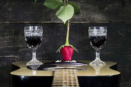 红玫瑰和酒杯搁在木吉他上