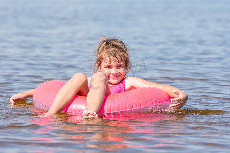 游泳画面摄影照片_五岁女孩在河里游泳，坐在腿上游泳，快乐地看着画面