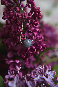 银色项链摄影照片_项链由天然石材制成，银色配件，白色鸵鸟羽毛上有紫色紫丁香花。