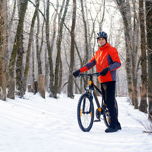在美丽的冬季森林的雪道上骑自行车的山地自行车手
