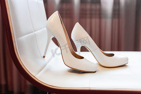 一双白色高跟鞋放在米色椅子上。
