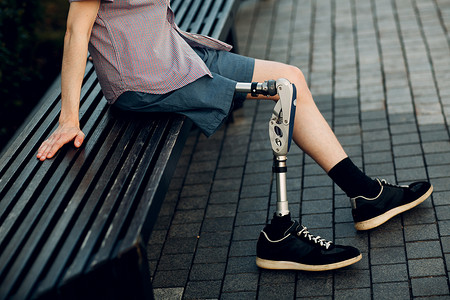 残疾人摄影照片_有脚假肢的残疾年轻人坐在室外