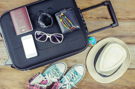 着装旅行者的护照、钱包、眼镜、手表、智能手机设备、帽子、鞋子，放在木地板上准备旅行的行李上。