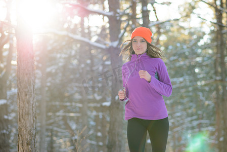奔跑乌龟摄影照片_在阳光明媚的寒冷日子里，年轻女子在美丽的冬季森林中奔跑。